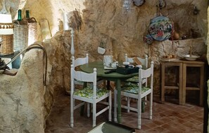 A rustic dining area with a stone wall, a round table, white chairs, and a small cabinet. - 1 bedroom beautiful home in Palazzolo Acreide (Palazzolo Acreide)