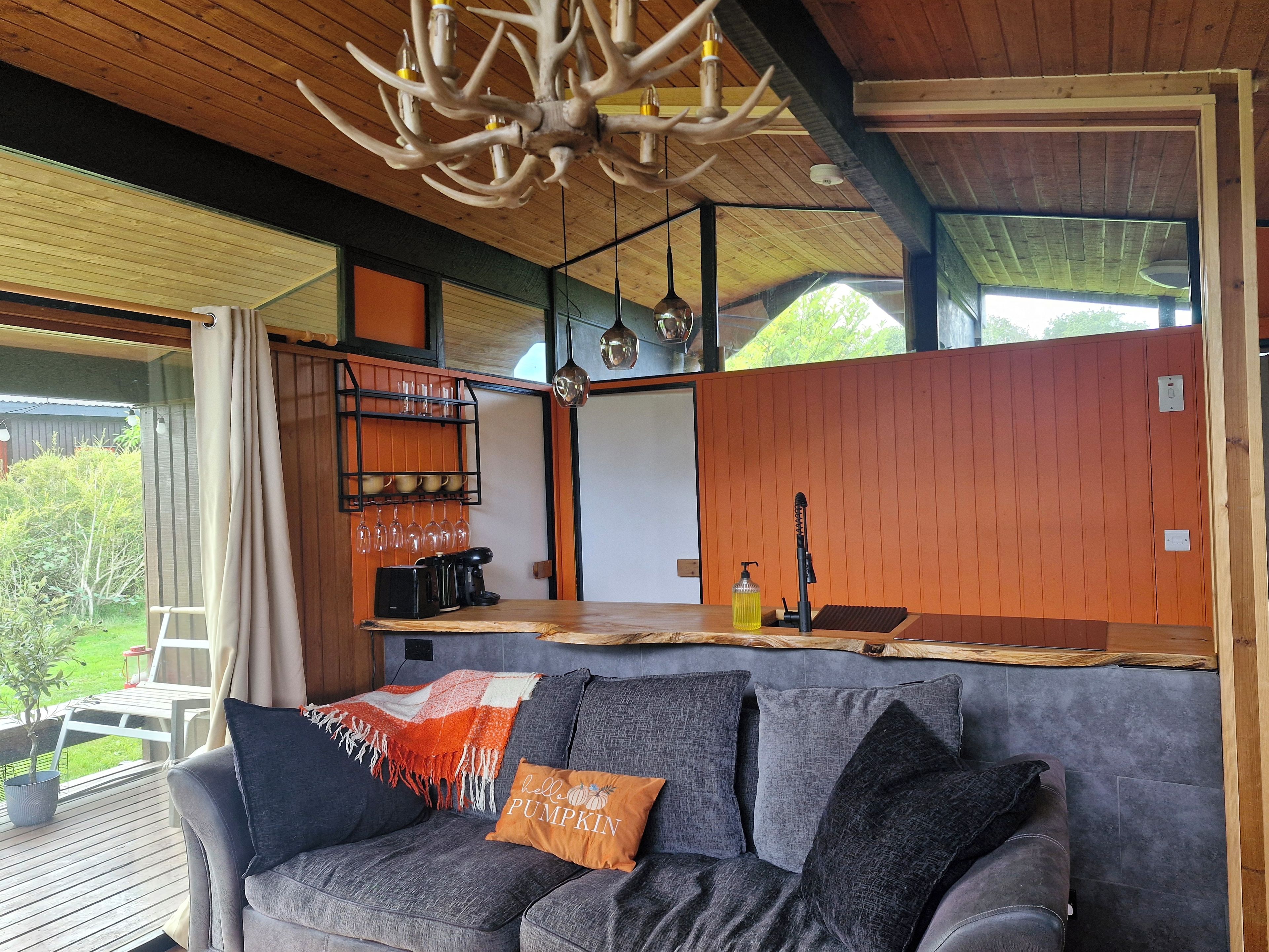 A cozy living area with a sofa, a coffee table, and a dining table. There is a chandelier above the dining table and a window providing a view of the outdoors.