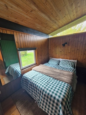A room with wooden walls, a window, a bed with checkered bedding, and a green door.