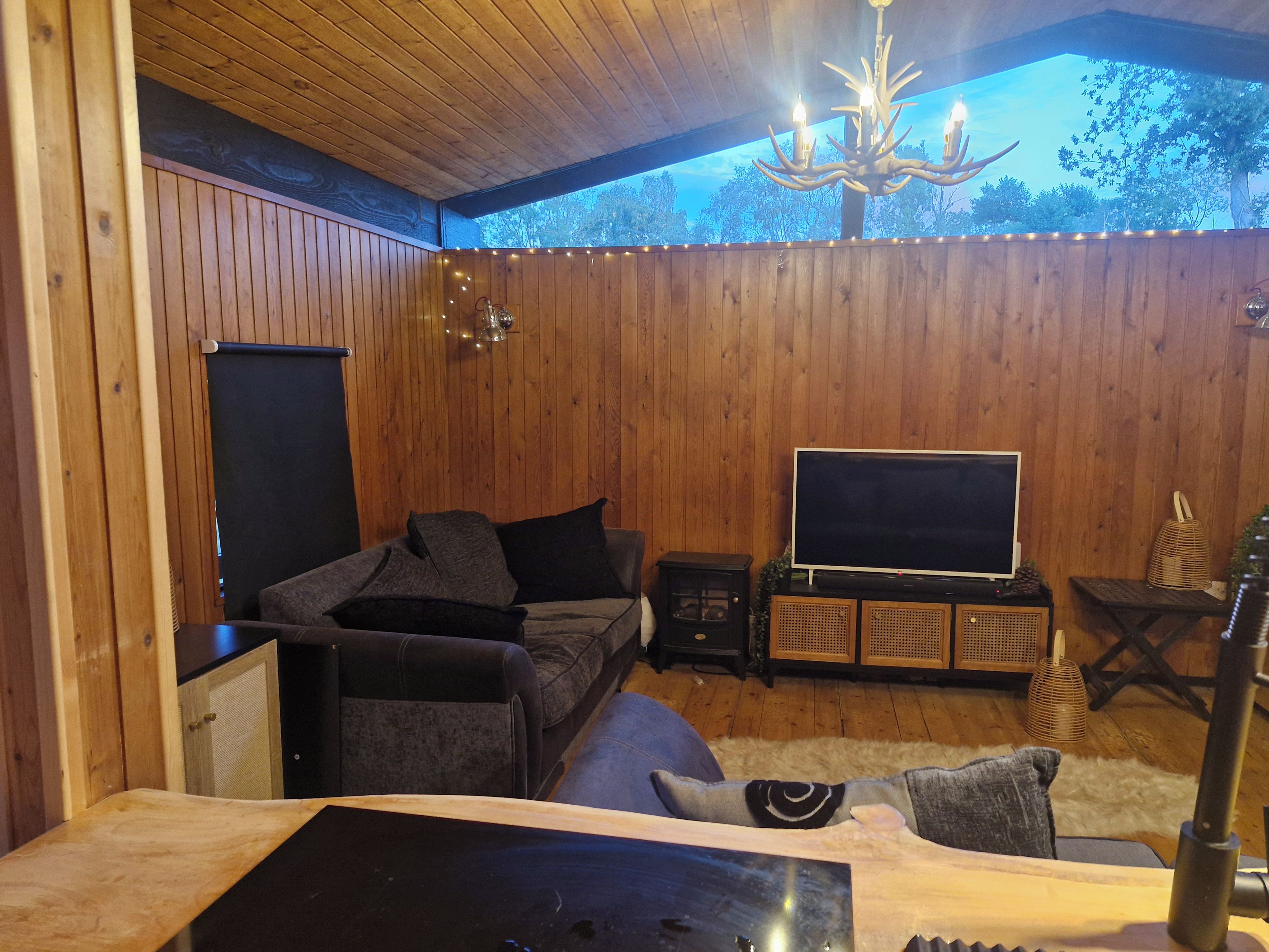 Um quarto aconchegante com paredes de madeira, um sofá, uma televisão e um candelabro.
