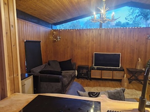 A cozy room with wooden walls, a sofa, a television, and a chandelier.