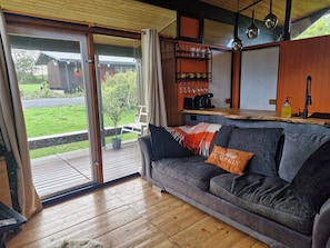A cozy living area with a sofa, a coffee table, and a view of a garden through a sliding glass door. - Cozy 3-Bed Chalet at Penlan Holiday Park | Pool (seasonal), WiFi & Dog Friendly (Cenarth)