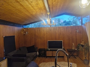 A cozy room with wooden walls, a ceiling fan, a TV, a sofa, and a small table with a lamp. - Cozy 3-Bed Chalet at Penlan Holiday Park | Pool (seasonal), WiFi & Dog Friendly (Cenarth)