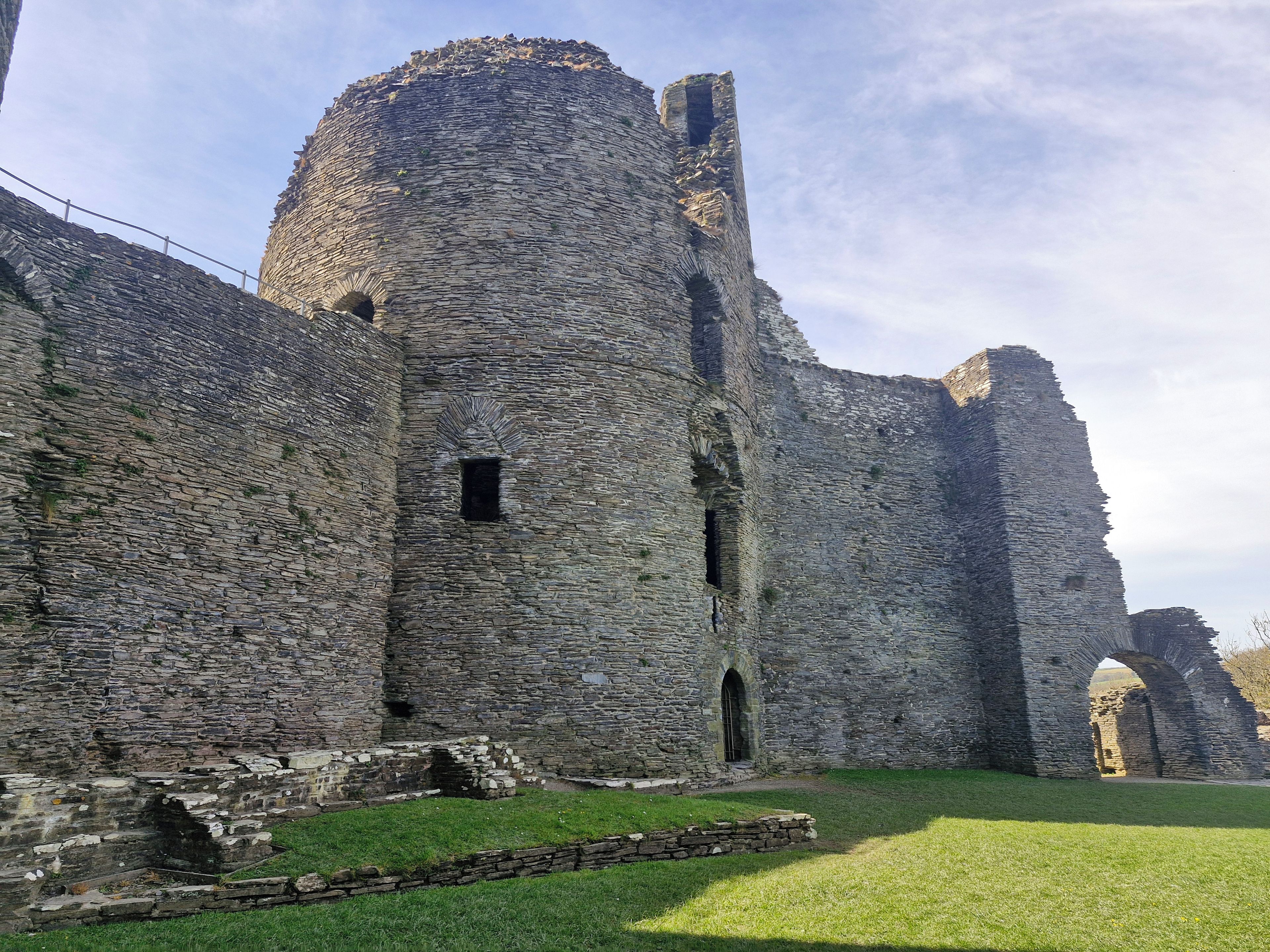 A historic stone castle with a large central tower, arched windows, and a grassy courtyard.