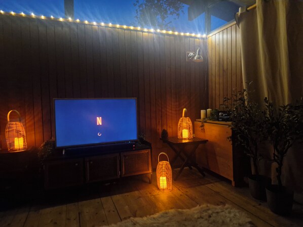 A wooden deck with a TV, two lantern-style lights, and a small table with candles.
