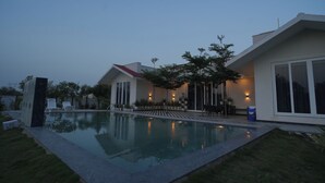 A modern house with a swimming pool, a covered patio, and a well-maintained lawn. - Luxury 3BHK Farmhouse Near Jaipur with Private Pool & Garden (jaipur)