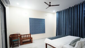 A bedroom with a bed, a ceiling fan, a small table with a chair, and a patterned wall. - Luxury 3BHK Farmhouse Near Jaipur with Private Pool & Garden (jaipur)