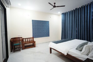A bedroom with a bed, a ceiling fan, a small table with a chair, and a patterned wall. - Luxury 3BHK Farmhouse Near Jaipur with Private Pool & Garden (jaipur)