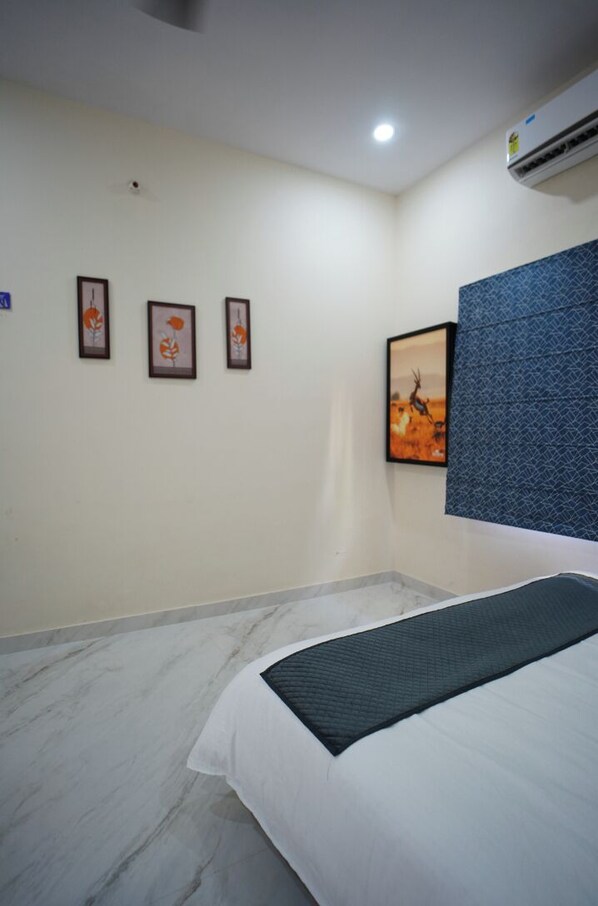 A hotel room with a bed, a wall-mounted air conditioner, and framed artwork on the wall.