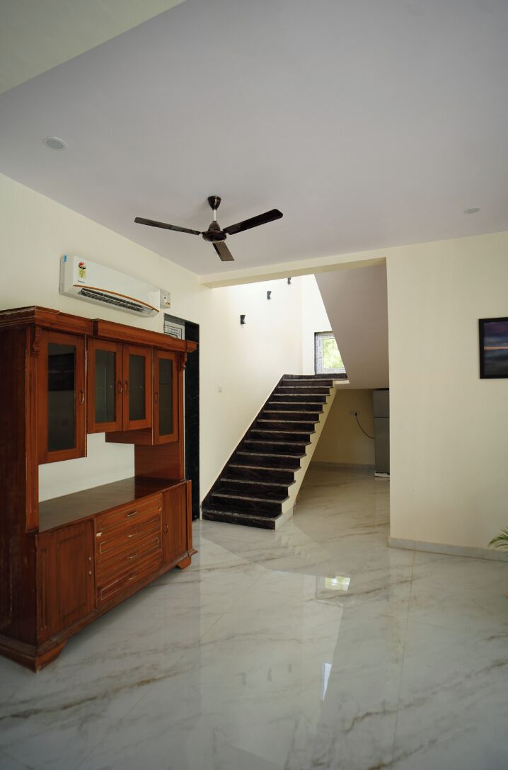 A spacious room with a marble floor, a wooden cabinet, a ceiling fan, and a staircase leading to another level.