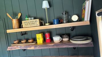 A kitchen with wooden shelves, a coffee maker, a kettle, and a sign for Spitalfields Old Market.