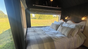 A bed with a view of a grassy field through a window, a bedside table, and a lamp. - Literally do Nothing but Relax & Unwind (Worcester)