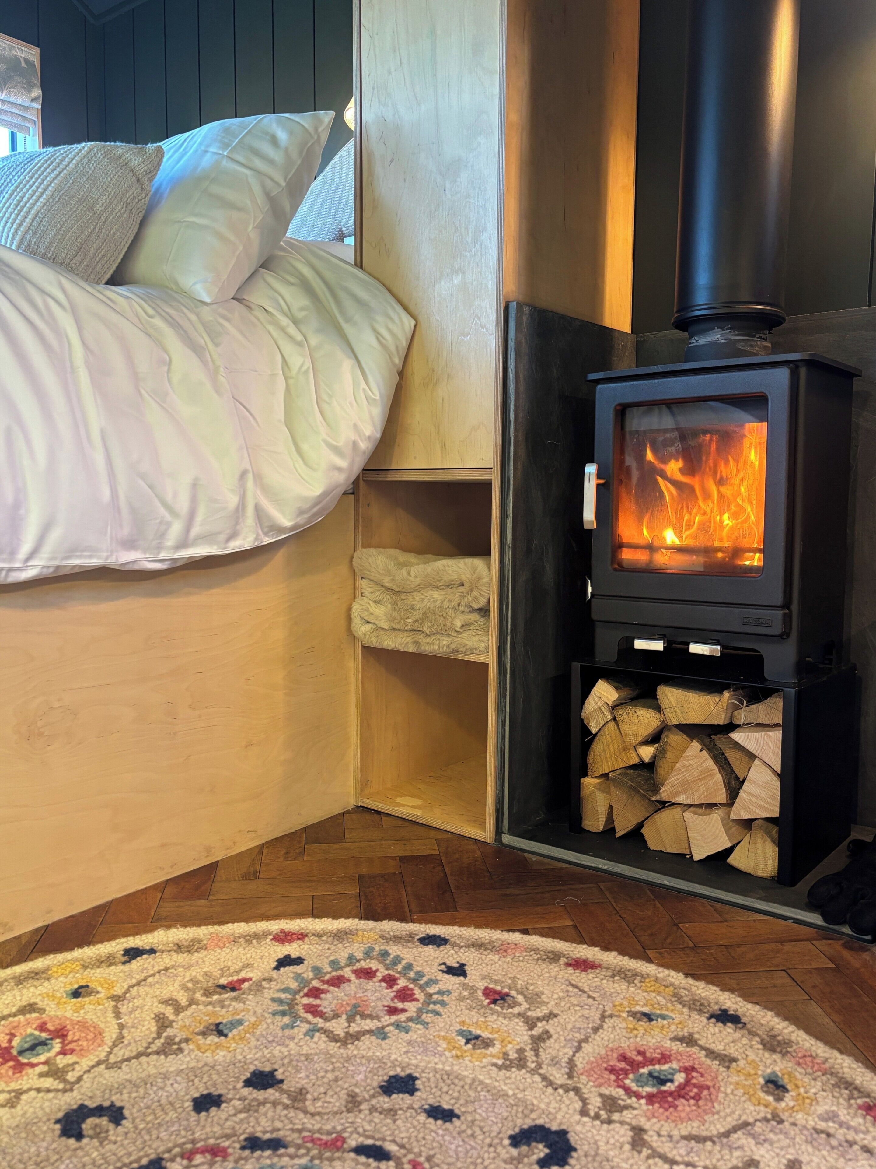 A cozy room with a bed, a wood-burning stove, and a patterned rug.