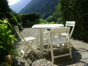 Conjunto de mesa e cadeiras brancas em superfície de cascalho, com montanhas ao fundo.