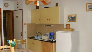 Eine kleine Küche mit Holzschränken, einem Kühlschrank, einer Kaffeemaschine und einem Esstisch mit Stühlen.