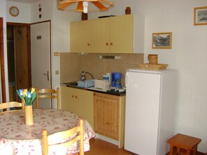 Cozinha compacta com armários de madeira, geladeira, cafeteira e mesa de jantar com cadeiras.