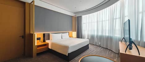 Habitación de hotel con cama, mesita de noche, lámpara, televisor y vistas al exterior.