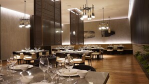 Un restaurante con varias mesas dispuestas para comensales, que presenta un diseño interior moderno con piso de madera e iluminación contemporánea.