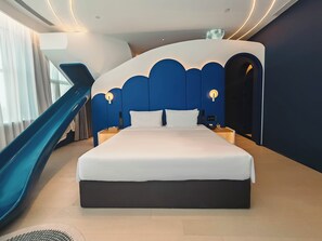 A modern hotel room with a large bed, a nightstand, a wall-mounted phone, and a control panel.