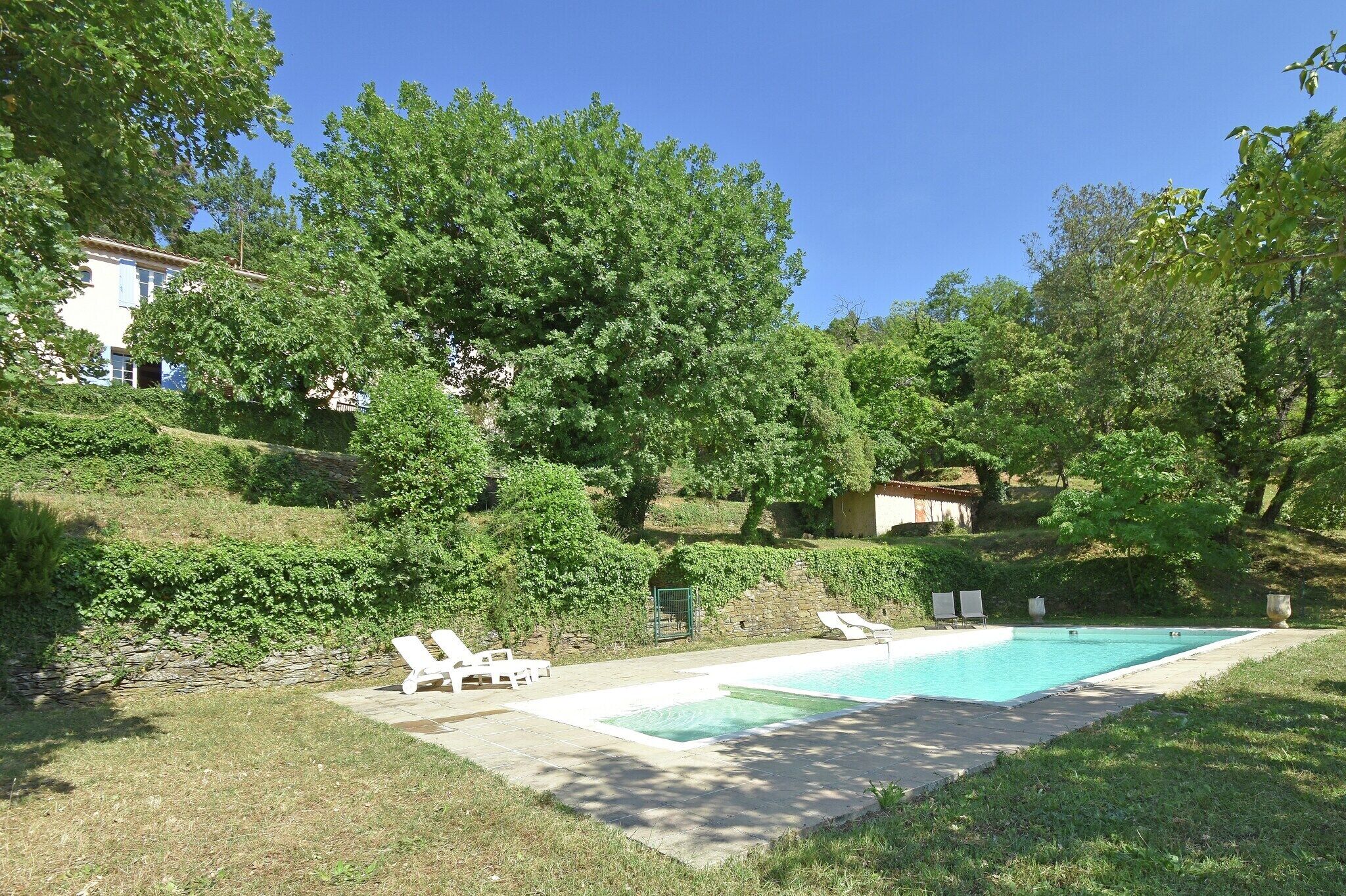 Une piscine entourée de chaises longues, de verdure et d’un mur en pierre.