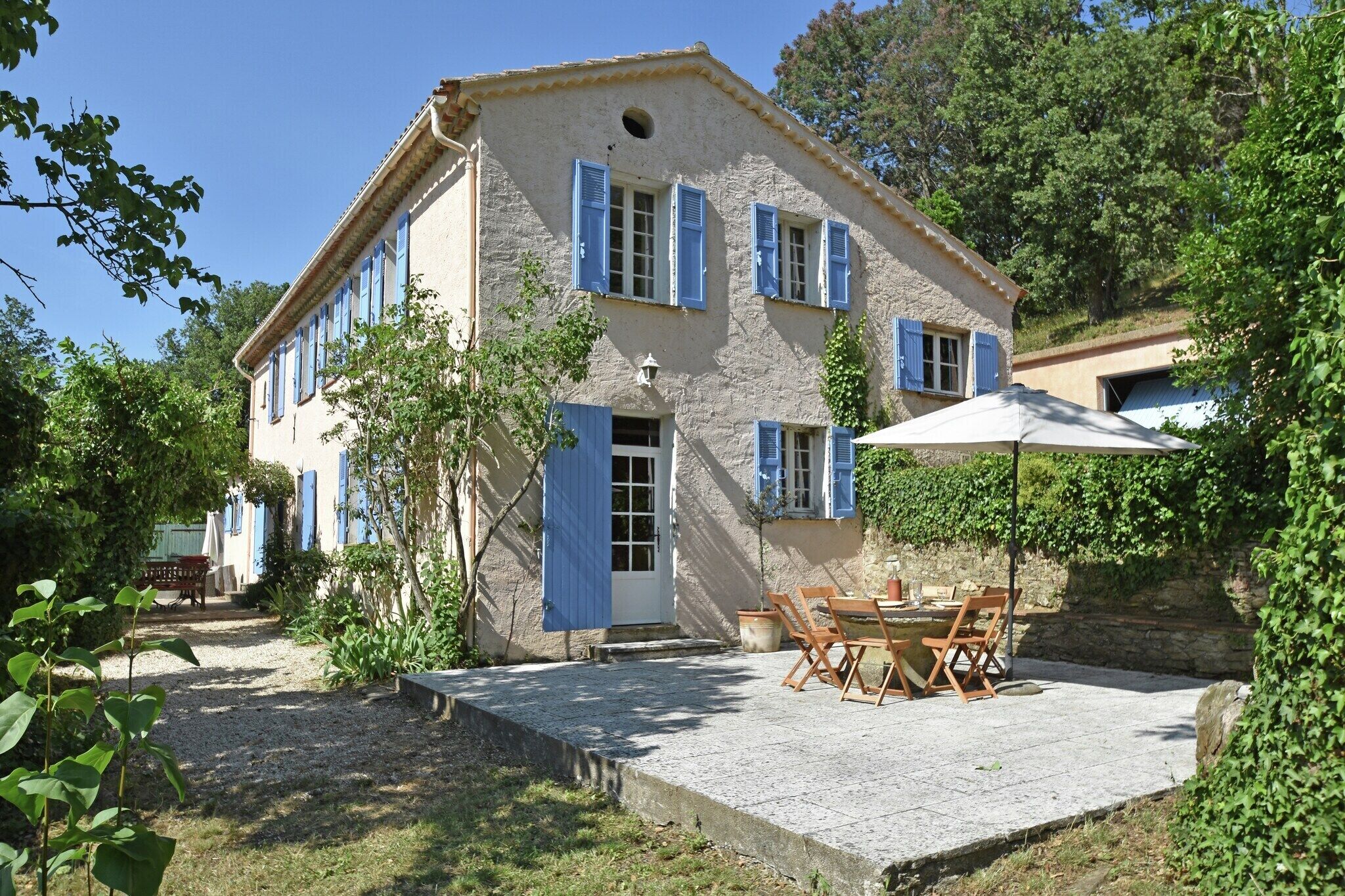 A two-story building with a stone facade, blue shutters, and a patio with outdoor furniture.