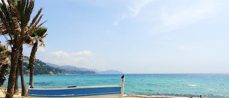 A beach with a boat, palm trees, and a clear sky.