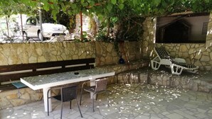 An outdoor patio with a stone floor, a table with chairs, a bench, and a grill area. - Apartments Katarina -one Bedroom Apartment With Terrace (Vis)