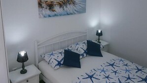 A bedroom with a bed, two bedside tables, a nightstand, a painting of a lighthouse, and star-patterned bedding. - Apartments Katarina -one Bedroom Apartment With Terrace (Vis)
