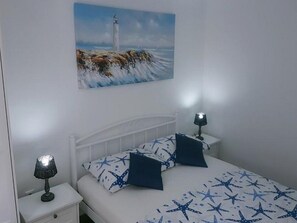 Ein Schlafzimmer mit einem Bett, zwei Nachttischen, einem Wandbild von einem Leuchtturm und Bettwäsche mit Sternenmuster.