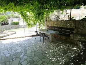 Eine Terrasse im Freien mit Steinboden, einem Tisch, Stühlen und einer Bank.