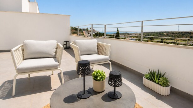 Eine Dachterrasse mit zwei Korbstühlen, einem runden Tisch, zwei schwarzen Lampen und Blumentöpfen.