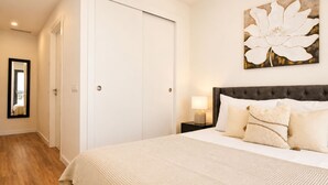 Ein Hotelzimmer mit einem großen Bett, einem Nachttisch mit Lampe, einer Tür und einem gerahmten Kunstwerk an der Wand.