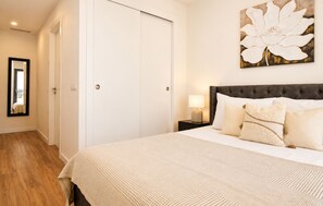 Ein Hotelzimmer mit einem großen Bett, einem Nachttisch mit Lampe, einer Tür und einem gerahmten Kunstwerk an der Wand.