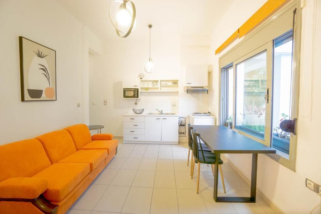 Un espacio habitable compacto con sofá, mesa de comedor, sillas, kitchenette y un ventanal grande.