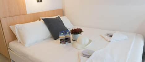 Ein ordentlich bezogenes Bett mit Kissen, ein kleiner Topfpflanze, ein Hut und ein gefaltetes Handtuch.
