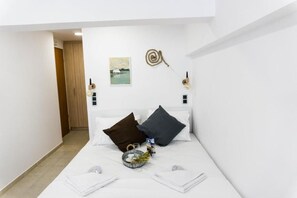 A hotel room with a bed, pillows, a bedside table, a wall-mounted light, and a painting.