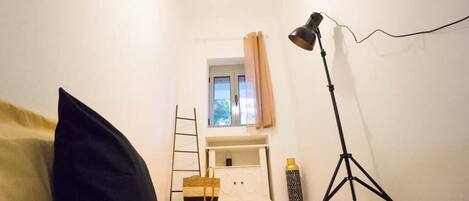 A room with a bed, a desk, a lamp, a ladder, and a window with curtains.