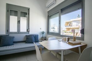 A modern room with a sofa, a dining table, and a large window offering a view of buildings.