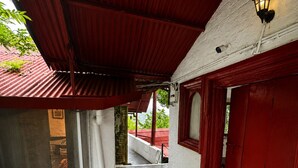 Un espacio al aire libre cubierto con piso de baldosas, una puerta roja y una pared blanca.