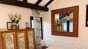 Una habitación con un armario de madera con puertas decoradas, un espejo con marco floral y una cortina estampada.