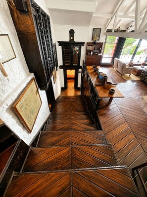 Una escalera con patrón de espiga conduce a una habitación con chimenea, muebles de madera y vistas al exterior.