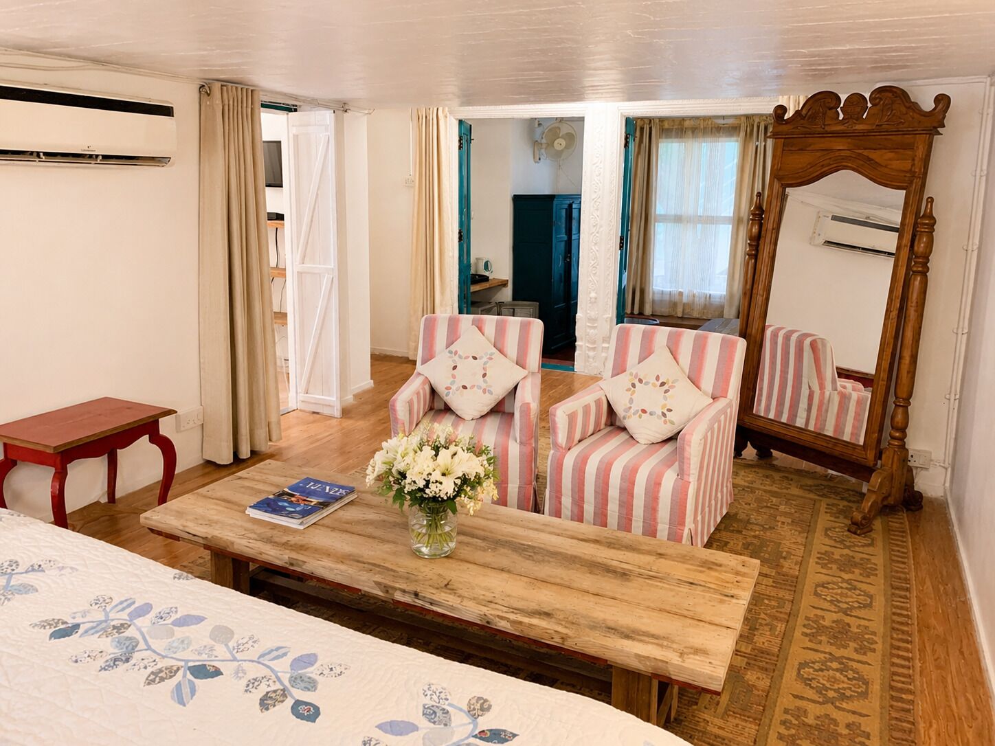 Une pièce avec des fauteuils à rayures, une table en bois ornée d’un vase de fleurs, une table rouge et un grand miroir.