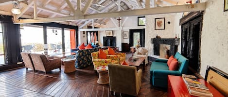 A spacious room with wooden flooring, a fireplace, and various seating arrangements including sofas and armchairs.