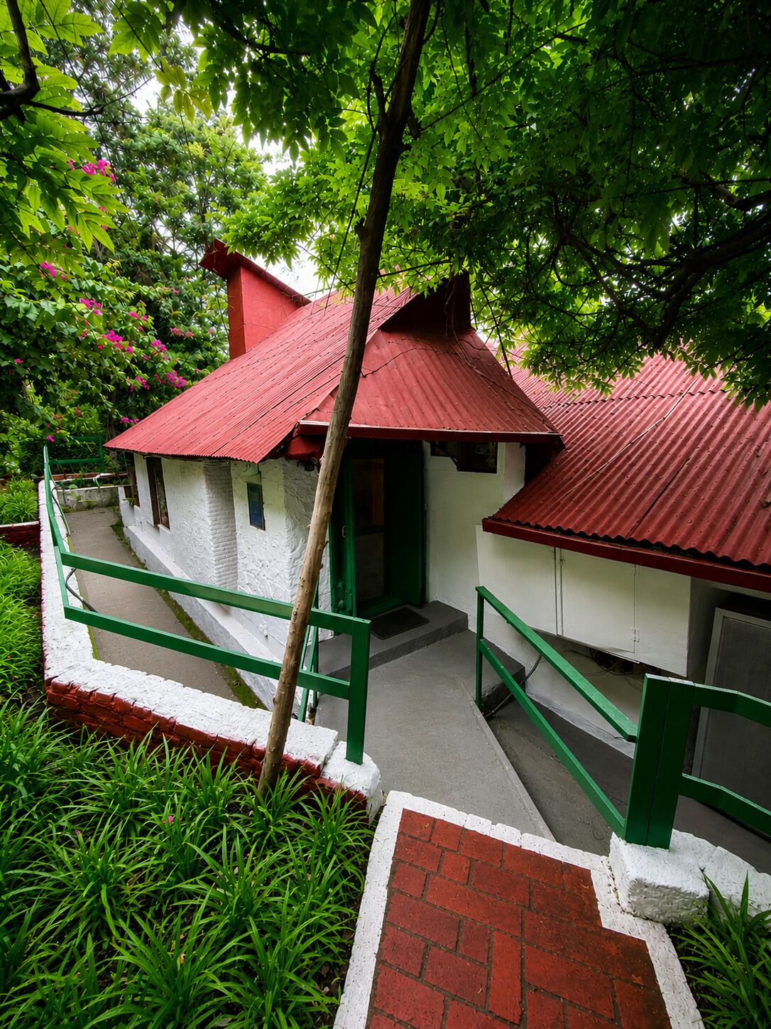 A building with a red roof and white walls, surrounded by greenery.