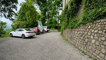 A gravel driveway leading to a building with a stone wall on one side and trees in the background.