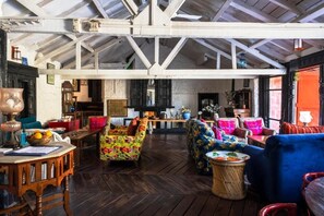 Un loft espacioso con vigas de madera a la vista, piso con dibujo de espiga y una mezcla de mobiliario tapizado de colores.