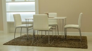 Un coin repas avec une table blanche et quatre chaises, un tapis marron et une bibliothèque blanche en arrière-plan.