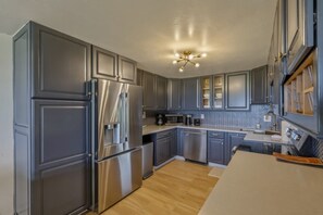 A modern kitchen with grey cabinets, stainless steel appliances, and a herringbone tile backsplash. - Fully Renovated Luxury Condo | Ocean Views + AC (Kailua-Kona)