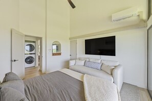 Un dormitori amb un llit, una televisió penjada a la paret i una rentadora a l'habitació veïna.