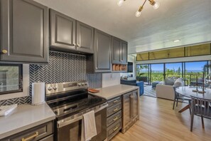 A modern kitchen with a large island, built-in appliances, and a view to a balcony. - Fully Renovated Luxury Condo | Ocean Views + AC (Kailua-Kona)